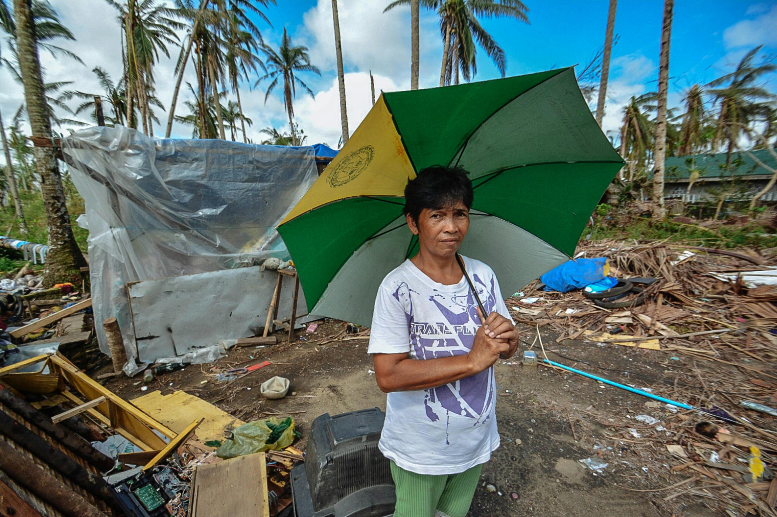 Asian woman holding an umbrella amidst storm aftermath with scattered debris.
