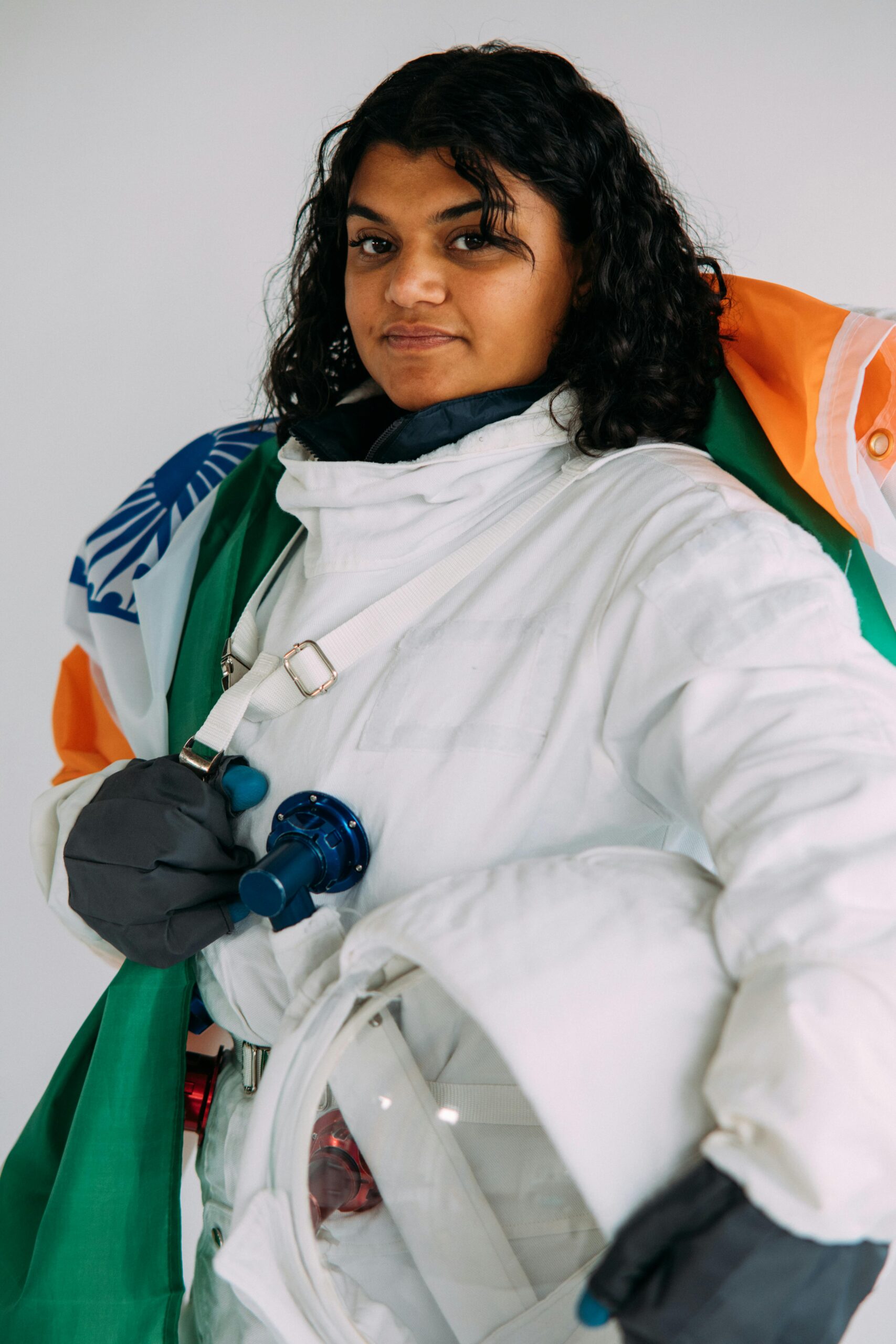 A confident South Asian woman in astronaut suit holding an Indian flag, conveying empowerment and diversity.